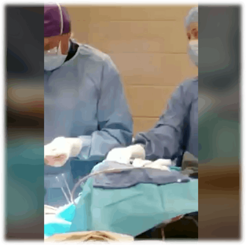 Two surgeons in blue gowns and masks working on a patient.